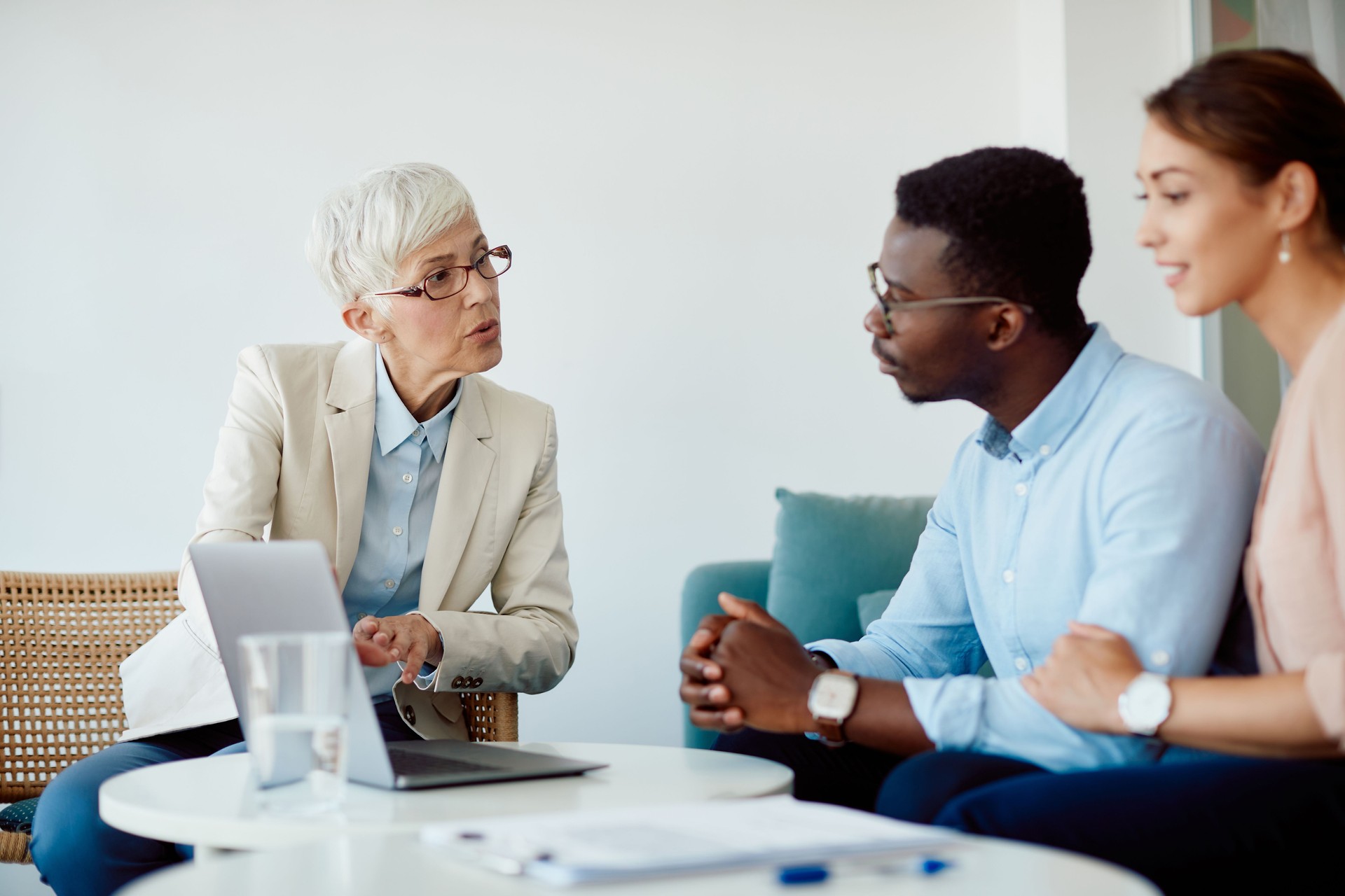 Senior financial advisor using laptop while talking to young couple in the office.